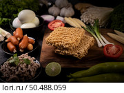 Noodles on a wooden cutting board with tomato, lime, spring onion, chili and baby corn. Стоковое фото, агентство Ingram Publishing / Фотобанк Лори