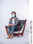 An uncomfortable woman sitting on a chair and wearing a mask. Стоковое фото, агентство Ingram Publishing / Фотобанк Лори