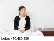 An uncomfortable woman sits on the bed and has medicine on the table. Стоковое фото, агентство Ingram Publishing / Фотобанк Лори