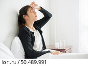 An uncomfortable woman sits on the bed and has medicine on the table. Стоковое фото, агентство Ingram Publishing / Фотобанк Лори