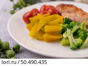 Chicken steak topped with white sesame, peas, tomatoes, broccoli and pumpkin in a white plate. Стоковое фото, агентство Ingram Publishing / Фотобанк Лори