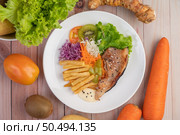 Fish steak with french fries, kiwi, lettuce, carrots, tomatoes, and cabbage in a white dish. Стоковое фото, агентство Ingram Publishing / Фотобанк Лори
