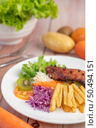 Fish steak with french fries, kiwi, lettuce, carrots, tomatoes, and cabbage in a white dish. Стоковое фото, агентство Ingram Publishing / Фотобанк Лори