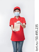 Image of a happy young delivery man in red cap blank t-shirt uniform face mask gloves standing with empty brown craft paper packet isolated on light gray background studio, Service during pandemic coronavirus virus covid-19 concept. Стоковое фото, агентство Ingram Publishing / Фотобанк Лори