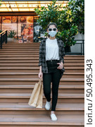 Portrait of young Asian woman wearing eyeglasses and protection mask going down stairs with shopping paper bag. Lifestyle and shopping concept. Стоковое фото, агентство Ingram Publishing / Фотобанк Лори
