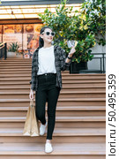 Portrait of young Asian woman wearing eyeglasses going down stairs with shopping paper bag. she smile and show credit card in hand,  Lifestyle and shopping concept. Стоковое фото, агентство Ingram Publishing / Фотобанк Лори