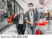 Young couple in protection mask holding multiple paper shopping bag walking in the corridor of large shopping mall, New normal lifestyle and shopping concept. Стоковое фото, агентство Ingram Publishing / Фотобанк Лори