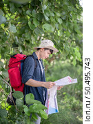 Young backpacker man wearing hat with map for checking direction,  He carry large backpack during relaxing outdoor on summer vacations in forest trial, copy space. Стоковое фото, агентство Ingram Publishing / Фотобанк Лори