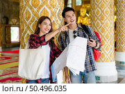 Happy Asian couple tourist backpackers holding paper map and looking for direction while traveling in Thai temple on holidays in Thailand, pretty woman pointing target . Стоковое фото, агентство Ingram Publishing / Фотобанк Лори
