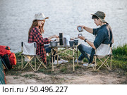 Cheerful Young backpacker couple wearing trekking hat sitting near lake with coffee and breakfast and making fresh coffee grinder while camping trip on summer vacation. Стоковое фото, агентство Ingram Publishing / Фотобанк Лори