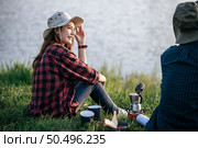 Cheerful Young backpacker couple sitting on grass and looking forward over lake in early morning and making fresh coffee grinder while camping trip on summer vacation. Стоковое фото, агентство Ingram Publishing / Фотобанк Лори