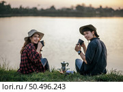 Cheerful Young backpacker couple sitting on grass near lake in early morning and making fresh coffee grinder while camping trip on summer vacation. Стоковое фото, агентство Ingram Publishing / Фотобанк Лори