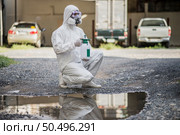 Portrait Disinfection specialist man in PPE suit, gloves, mask and face shield performing public decontamination, sitting and  holding bottle for spray disinfectant to remove covid-19  . Стоковое фото, агентство Ingram Publishing / Фотобанк Лори