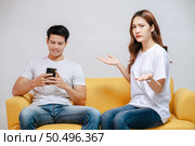 young couple arguing while handsome man using mobile phone on sofa in living room at home. husband addict On Mobile Phone Ignoring her, upset couple, family issues and relationship concept. Стоковое фото, агентство Ingram Publishing / Фотобанк Лори