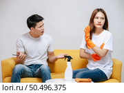 Asian young couple quarrels while cleaning in the living room, Young woman wearing gloves and holding spray bottle in hand with feel dissatisfied her husband, family issues and relationship concept. Стоковое фото, агентство Ingram Publishing / Фотобанк Лори