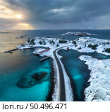 Aerial view of road, island in snow, rorbu, sea, bridge, snowy mountains, azure water, cloudy sky at sunset in winter. Dramatic landscape. Top drone view of road. Henningsvaer, Lofoten islands, Norway. Стоковое фото, агентство Ingram Publishing / Фотобанк Лори