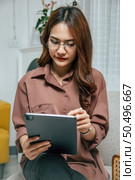 Young woman wearing glasses using technology of digital pen on tablet to working from home during self-isolation and quarantine covid-19 coronavirus outbreak. Стоковое фото, агентство Ingram Publishing / Фотобанк Лори