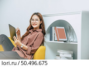 Young woman wearing glasses sitting on sofa and using technology of digital pen on tablet to working from home during self-isolation and quarantine covid-19 coronavirus outbreak. Стоковое фото, агентство Ingram Publishing / Фотобанк Лори
