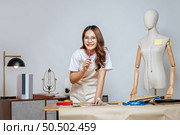 Portrait of young pretty female fashion designer stylish wearing eyeglasses standing and smile with proud during working at fashion studio, full of tailoring tools and equipment. Стоковое фото, агентство Ingram Publishing / Фотобанк Лори