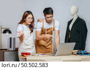 Young handsome man and pretty woman, Couple designer has conflict together while use laptop computer chatting with customer online order, mannequin and tailoring tools on desk. Стоковое фото, агентство Ingram Publishing / Фотобанк Лори