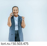Portrait of Asian woman keeps hands clenched in fists with positiveness as achieved success in career, smiling widely, showing strong powerful while talking on mobile isolated over background. Стоковое фото, агентство Ingram Publishing / Фотобанк Лори