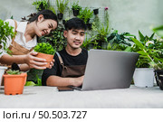 Happily gardener couple use laptop computer while online tutorial on potted plans in workshop together, vlogging or small business houseplant concept. Стоковое фото, агентство Ingram Publishing / Фотобанк Лори