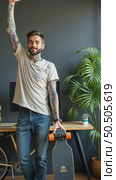 Tattooed lucky freelancer in front of his working space, surrounded with his hobby toys longboard, vintage bicycle and green plant, stretching his hand in air. Стоковое AI-видео, аниматор Sergey Grishin / Фотобанк Лори