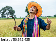 Happily young farmer wearing straw hat and loincloth standing with thump up and holding sickle in rice field. Стоковое фото, агентство Ingram Publishing / Фотобанк Лори