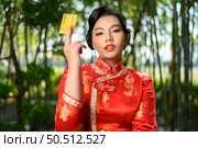 Portrait beautiful Asian woman in a Chinese cheongsam pose with credit card on bamboo forest background, copy space, Chinese New Year concept. Стоковое фото, агентство Ingram Publishing / Фотобанк Лори