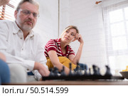 In the living room of the house, an elderly couple sits and relaxes. to begin playing chess together with a chess board with a daughter cheering beside him. Стоковое фото, агентство Ingram Publishing / Фотобанк Лори