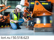 Female Technician Inspecting and repairing robotics arm in robots hangar and test the operation of the machine after being used for a while, as well as updating the software and calibration. Стоковое фото, агентство Ingram Publishing / Фотобанк Лори