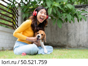 Young asian woman and beagle puppy relaxing on weekends in the front yard. Стоковое фото, агентство Ingram Publishing / Фотобанк Лори