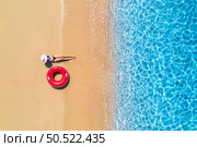 Aerial view of a lying woman in hat with red swim ring on sandy beach and blue sea at sunset in summer. Tropical landscape with girl, ocean with clear water, waves. Top view. Sardinia island, Italy. Стоковое фото, агентство Ingram Publishing / Фотобанк Лори