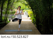 Young female in the garden there are wooden walkways and a tunnel of fresh green trees, with yoga activities for health. Стоковое фото, агентство Ingram Publishing / Фотобанк Лори