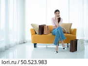 Portrait of young asian woman sitting on sofa in the shop’s VIP lounge with shopping bags. Стоковое фото, агентство Ingram Publishing / Фотобанк Лори