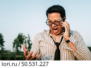Young funny Asian Businessman wearing shirt and tie with shorts and eyeglasses with smartphone in hand, shouting  crazy and funny manner posture, copy space. Стоковое фото, агентство Ingram Publishing / Фотобанк Лори