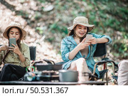 Selective focus, Group of girl friends sitting on camping chair and use their smartphone ignoring each other while camping in park. Стоковое фото, агентство Ingram Publishing / Фотобанк Лори