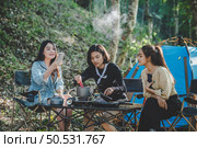 Young asian woman cooking and her friend enjoy to make the meal in pot, They are talk and laugh with fun together while camping in nature park. Стоковое фото, агентство Ingram Publishing / Фотобанк Лори
