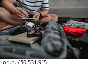 Asian man is preparing clothes in suitcases. He’s choosing clothes, travel documents, the itinerary for a solo trip, and check the checklist. Travel, holiday and vacation concept. Стоковое фото, агентство Ingram Publishing / Фотобанк Лори