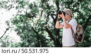 Asian traveler man with backpack taking a photo in the park with copy space. Travel photographer. Vocation and holiday concept. Стоковое фото, агентство Ingram Publishing / Фотобанк Лори