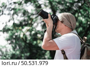 Asian traveler man with backpack taking a photo in the park with copy space. Travel photographer. Vocation and holiday concept. Стоковое фото, агентство Ingram Publishing / Фотобанк Лори