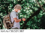 Asian Traveler man wears medical mask with backpack checking a picture on camera at the park with copy space. Travel photographer. Vocation and holiday concept. Стоковое фото, агентство Ingram Publishing / Фотобанк Лори