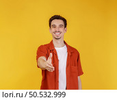 Portrait of smiling handsome man extend hand for handshake, look friendly, greet you, hi gesture, standing over yellow background. Стоковое фото, агентство Ingram Publishing / Фотобанк Лори