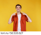 Portrait of young man pointing fingers at copy space isolated on yellow studio background. Smiling guy advertising product or service. Стоковое фото, агентство Ingram Publishing / Фотобанк Лори