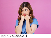 Portrait of thoughtful miserable dejected woman wearing casual t-shirt keeping hands under chin isolated over pink background. Expression, people and lifestyle concept. Стоковое фото, агентство Ingram Publishing / Фотобанк Лори