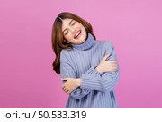 Portrait of Smiling young woman sweet winsome lovely attractive charming cheerful cheery lady hugging herself isolated over pink background. People lifestyle and expression concept. Стоковое фото, агентство Ingram Publishing / Фотобанк Лори