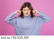 Portrait of Annoyed woman sticking plug fingers in ears not listening to loud noise sound isolated over pink background. Refuse hear avoid stress feel ear pain ache concept. Стоковое фото, агентство Ingram Publishing / Фотобанк Лори