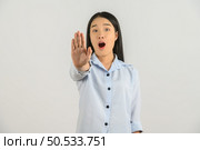 Portrait of Excited young asian woman in blue shirt showing hand foreground and looking at camera isolated on white background. Expression and lifestyle concept. Стоковое фото, агентство Ingram Publishing / Фотобанк Лори
