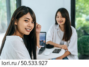 Close up portrait shot of beautiful young woman smiling and looking to camera with having wide toothy charming smile at coffee shop, blurred her girl friend smiling behind, laptop computer on desk. Стоковое фото, агентство Ingram Publishing / Фотобанк Лори