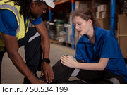 A warehouse worker consoles and helps a female worker who cries out in pain after a leg accident in a large warehouse. Стоковое фото, агентство Ingram Publishing / Фотобанк Лори